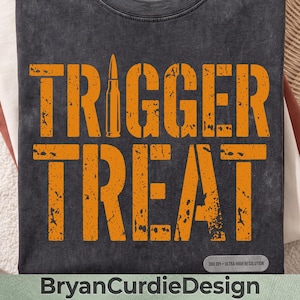 May include: A charcoal gray t-shirt with a distressed orange graphic print. The text reads TRIGGER TREAT, with a bullet icon replacing the letter I. The fabric has a washed, vintage appearance. A small rectangular label reads 300 DPI ULTRA HIGH RESOLUTION.