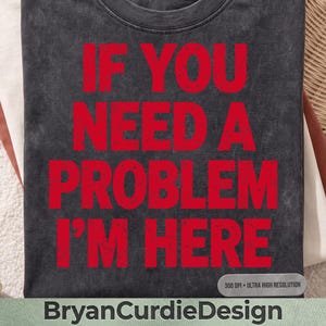Może przedstawiać: Ciemnoszary t-shirt z nadrukiem graficznym w kolorze wyblakłej czerwieni, zawierającym napis IF YOU NEED A PROBLEM I'M HERE pogrubionymi wielkimi literami. Materiał ma sprany wygląd w stylu vintage, a tekst jest wyśrodkowany na przodzie koszulki.