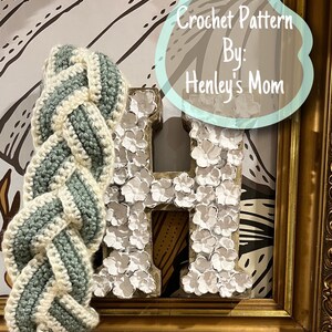 May include: A crochet pattern for a braided headband in green and white yarn. The pattern is titled "Crochet Pattern By: Henley's Mom".