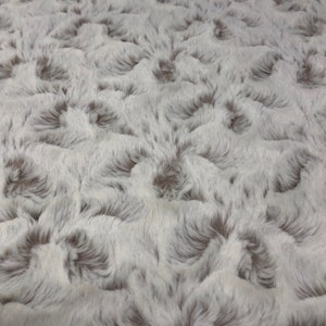 May include: White and gray faux fur fabric with a textured, swirling pattern. The fabric has a soft, plush feel.