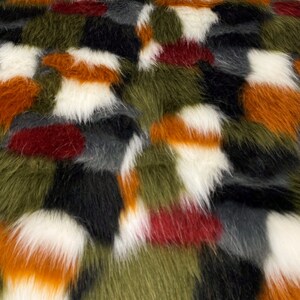 Pode incluir: Close-up de um tecido de pele sintética com um design de patchwork. O tecido apresenta uma mistura de cores, incluindo branco, preto, laranja, verde oliva, cinza e bordô. A pele tem um pelo longo e uma textura macia, adequada para vários projetos.