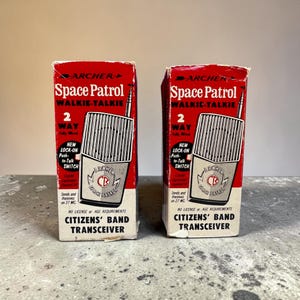 Könnte beinhalten: Zwei Vintage-Walkie-Talkie-Boxen "Space Patrol" in Rot und Weiß. Jede Box zeigt eine Grafik eines Walkie-Talkies und den Text "2 Way". Die Boxen sind mit "Citizens' Band Transceiver" beschriftet.