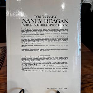 May include: A book titled "Nancy Reagan Fashion Paper Dolls in Full Color" by Tom Tierney. The cover features text and is a paperback. The book is a Dover publication from 1983.