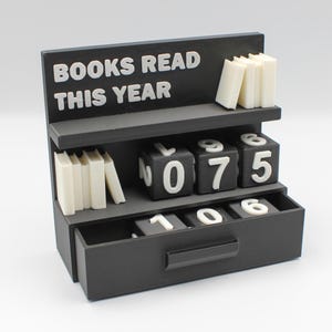 May include: A black bookshelf-shaped counter with the text "BOOKS READ THIS YEAR" in white. It has shelves with small book stacks and number blocks to track reading progress. The current count is 075.