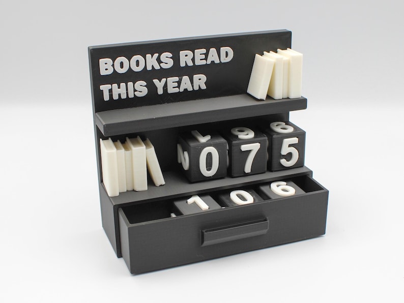 Puede incluir: Un contador negro con forma de estanter&iacute;a con el texto "BOOKS READ THIS YEAR" en blanco. Tiene estantes con peque&ntilde;as pilas de libros y bloques num&eacute;ricos para realizar un seguimiento del progreso de la lectura. La cuenta actual es 075.