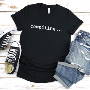 May include: Black t-shirt with the text "compiling..." in white.
