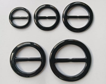 May include: Four black plastic buckle closures of different sizes. The buckles are round with a center bar.
