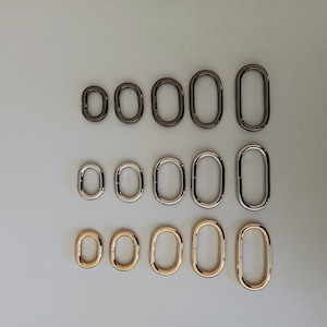 May include: A set of 12 metal rings in three different sizes and colours: silver, gold, and black. The rings are oval-shaped and have a smooth finish.