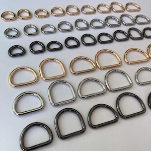 May include: Assortment of metal D-rings in various sizes and finishes, including gold, silver, and black.