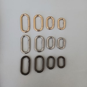 May include: Assortment of oval-shaped metal rings in gold and silver tones. The rings are different sizes and are arranged in rows.