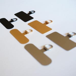 May include: Five metal hanging hardware pieces with a T-shaped base and a ring at the top. The pieces are in black, gold, and silver.