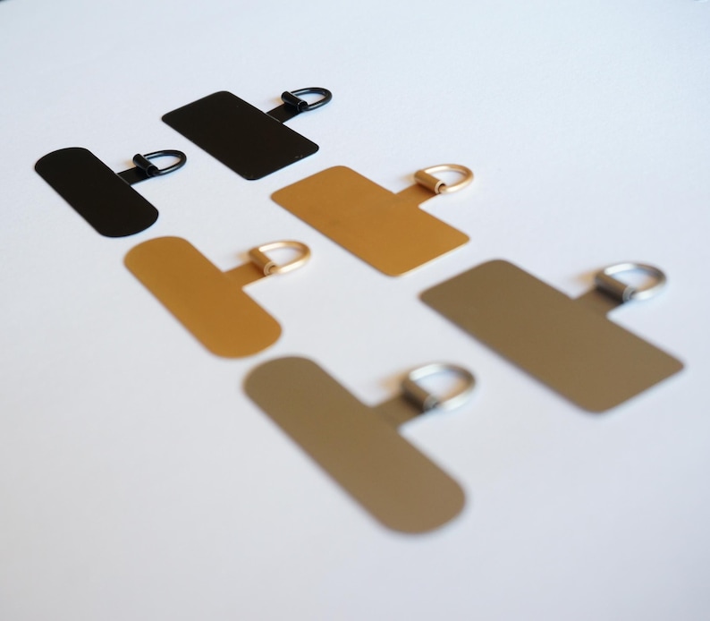 May include: Five metal hanging hardware pieces with a T-shaped base and a ring at the top. The pieces are in black, gold, and silver.