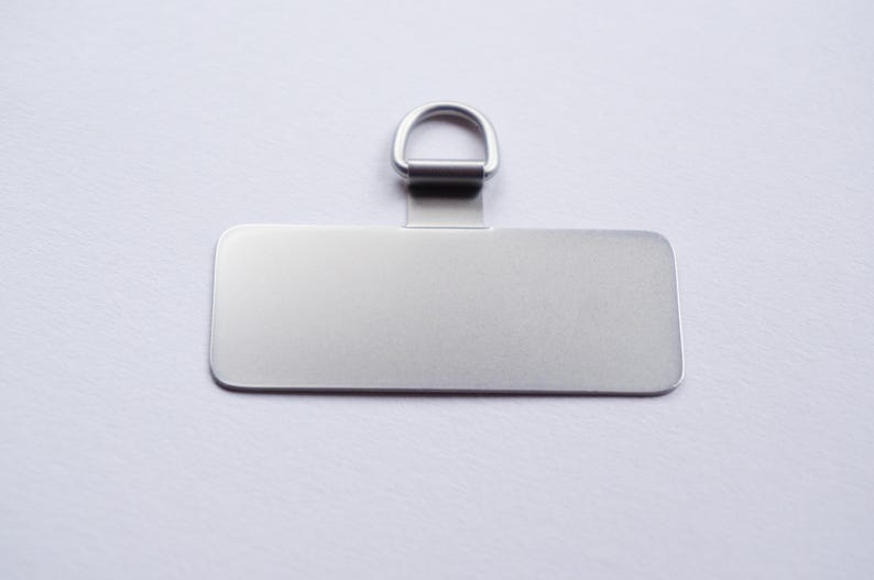 May include: A silver rectangular tag with a silver ring attached to the top. The tag is blank and ready to be personalized.
