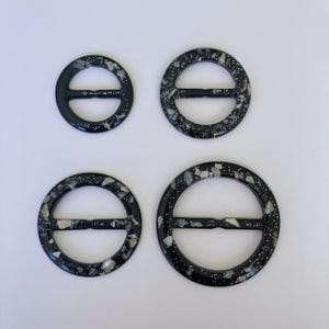 May include: Four black plastic belt buckles with a silver glitter finish. The buckles are round with a centre bar and come in different sizes.