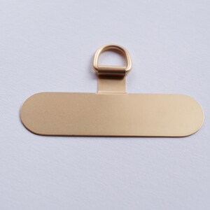 May include: A gold-colored metal tag with a rounded oval shape and a small ring at the top. The tag is blank and ready for personalization.