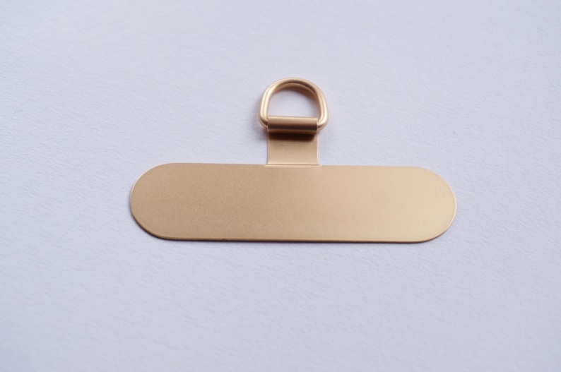 May include: A gold-colored metal tag with a rounded oval shape and a small ring at the top. The tag is blank and ready for personalization.