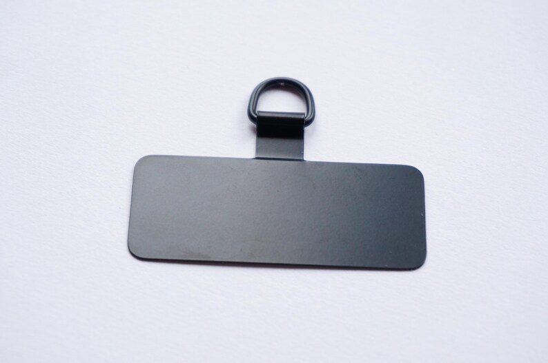 May include: A black metal tag with a rounded rectangular shape and a metal ring at the top.