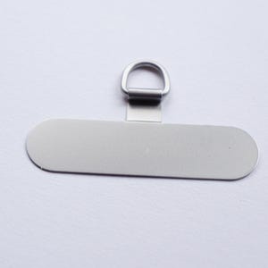 May include: A silver metal tag with a loop at the top. The tag is oval shaped and has a smooth surface.