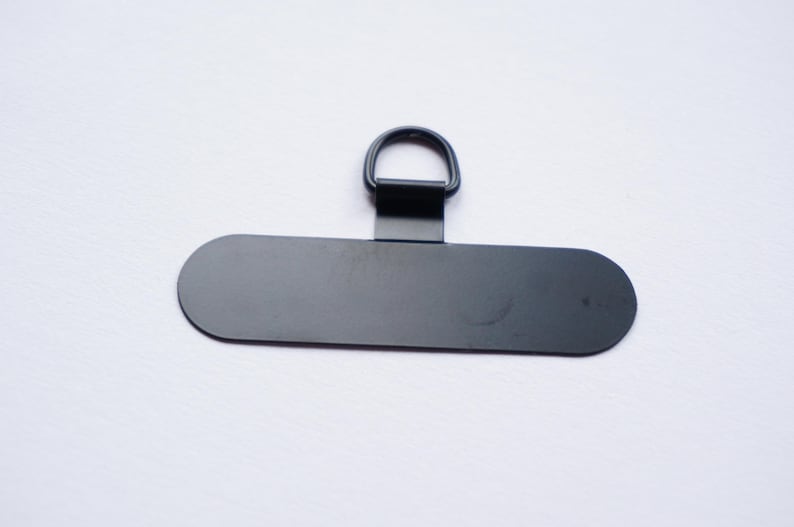 May include: Black metal hanging hardware with a D-ring and a flat rectangular plate.