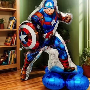 May include: A large Captain America foil balloon in a dynamic pose, holding his shield. The balloon features a detailed illustration in red, white, and blue, with a star on the shield. It is supported by several blue balloons, creating a festive display.