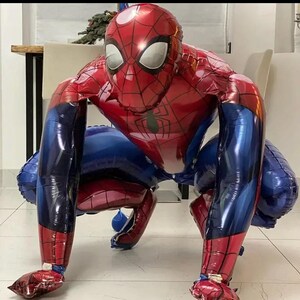 May include: A large, inflatable Spider-Man balloon in a crouching pose. The balloon features a red and blue color scheme, with a detailed web pattern on the red sections. The eyes are white, and the overall design is a faithful representation of the character.