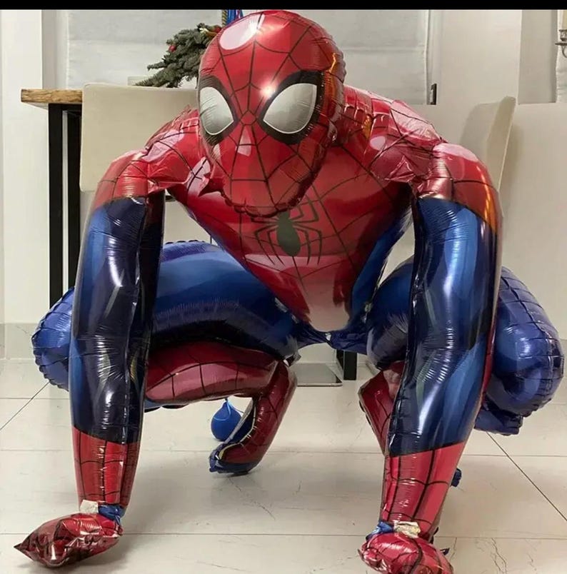 May include: A large, inflatable Spider-Man balloon in a crouching pose. The balloon features a red and blue color scheme, with a detailed web pattern on the red sections. The eyes are white, and the overall design is a faithful representation of the character.