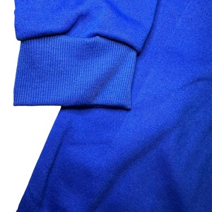 May include: A close-up of a royal blue sweatshirt with ribbed cuffs. The fabric is soft and textured.
