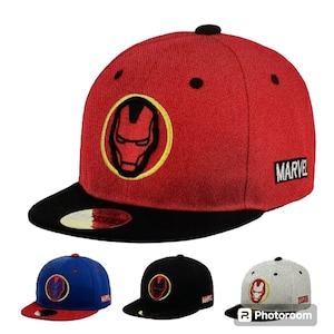 May include: Three baseball caps with a black and yellow Iron Man logo on the front. The caps are red, blue, and white with black brims. The word "MARVEL" is on the side of each cap.