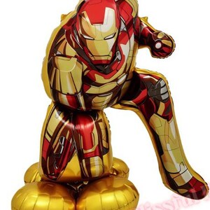 K&ouml;nnte beinhalten: Ein gro&szlig;er, metallisch goldener, roter und bronzefarbener Iron Man-Ballon in sitzender Pose. Der Ballon ist mit dem Helm und der R&uuml;stung der Figur detailliert. Die Basis des Ballons besteht aus mehreren goldfarbenen, abgerundeten Formen.