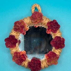 Pu&ograve; includere: Uno specchio circolare incorniciato da una spessa corda di iuta color naturale. La cornice &egrave; decorata con sette piante succulente artificiali in tonalit&agrave; profonde di bordeaux e rosso. Un piccolo cappio della stessa corda &egrave; fissato in alto.
