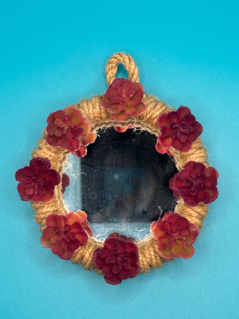 Pu&ograve; includere: Uno specchio circolare incorniciato da una spessa corda di iuta color naturale. La cornice &egrave; decorata con sette piante succulente artificiali in tonalit&agrave; profonde di bordeaux e rosso. Un piccolo cappio della stessa corda &egrave; fissato in alto.