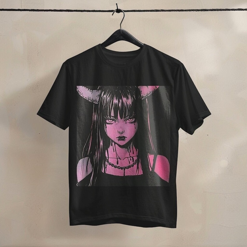 May include: Black t-shirt featuring a pink and black anime-style illustration of a female figure with horns, long black hair, and a chain necklace. The graphic has a dark, gothic aesthetic.