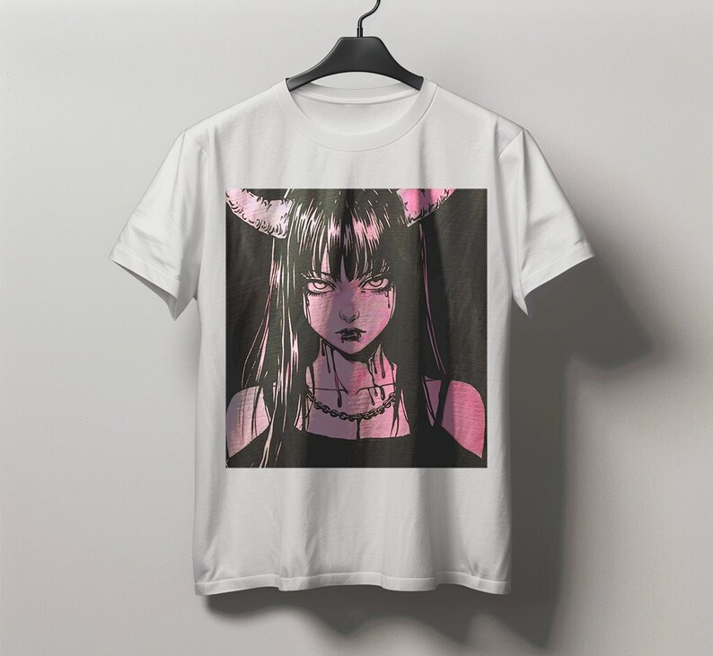 May include: White t-shirt featuring a pink and black anime-style illustration of a woman with long black hair, horns, and a necklace. The graphic has a dark, gothic aesthetic.