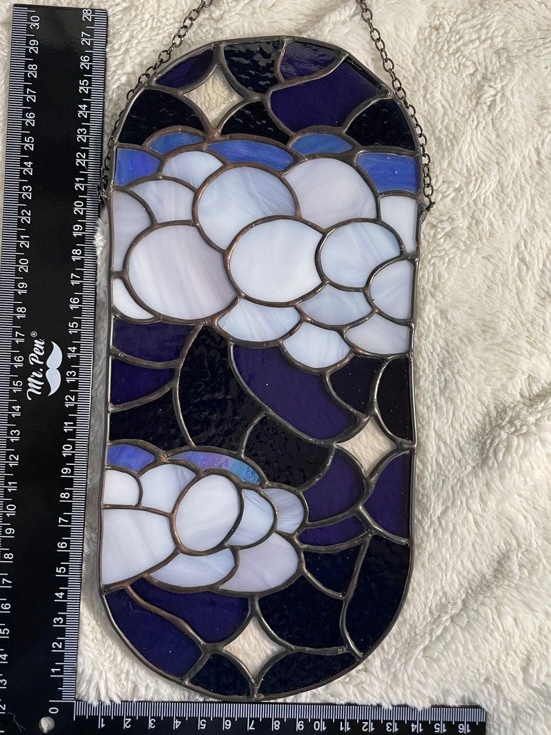 May include: A stained glass window hanging with a chain. The window is oval shaped and features a design of white and blue circles on a dark blue background.