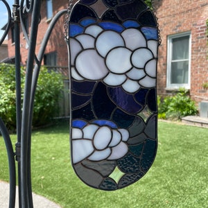 May include: A stained glass window hanging from a chain. The window is oval shaped and features a design of white flowers on a dark blue background.