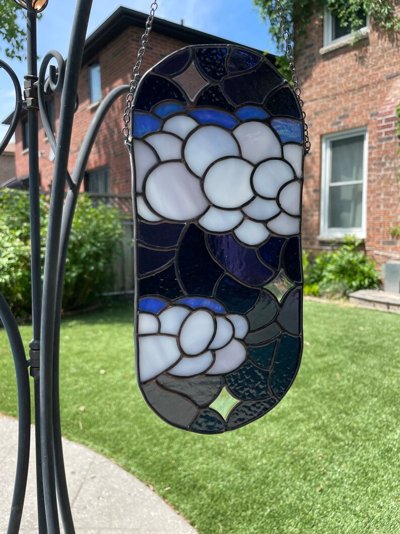 May include: A stained glass window hanging from a chain. The window is oval shaped and features a design of white flowers on a dark blue background.