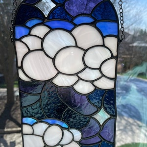 May include: A stained glass window hanging with a chain. The design features white clouds on a blue and purple background.