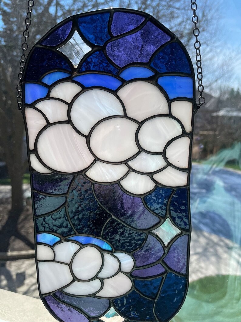 May include: A stained glass window hanging with a chain. The design features white clouds on a blue and purple background.