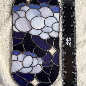 May include: A stained glass window hanging with a chain. The window is oval shaped and features a design of white and blue flowers on a dark blue background.
