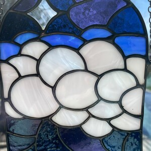 May include: A stained glass window hanging with a blue, purple, and white design. The design features a cloud-like shape with a star in the upper left corner.