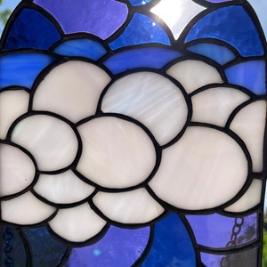 May include: A stained glass window depicting a blue sky with white clouds. The sky is made up of various shades of blue and purple glass, while the clouds are made of white opaque glass.