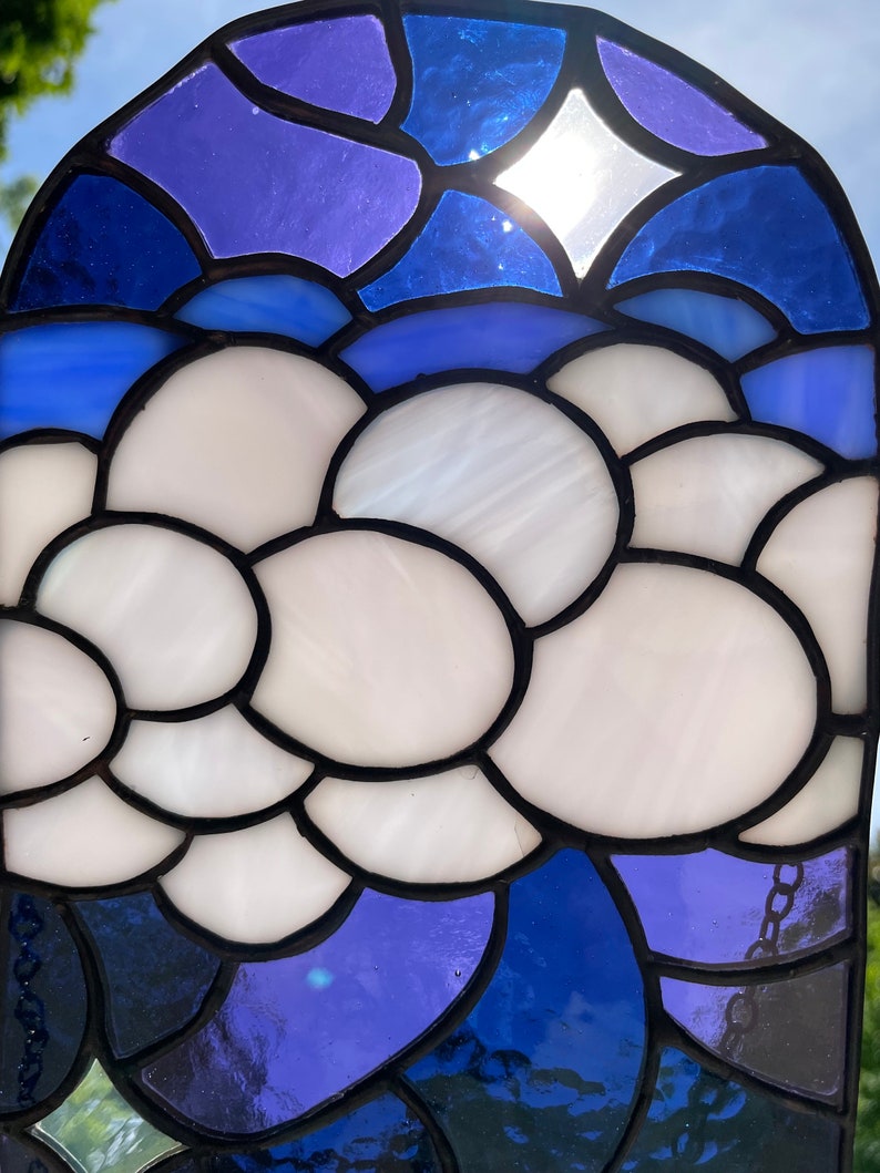 May include: A stained glass window depicting a blue sky with white clouds. The sky is made up of various shades of blue and purple glass, while the clouds are made of white opaque glass.