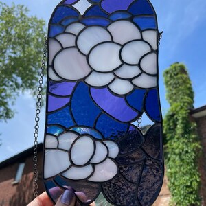 May include: A stained glass window hanging with a chain. The design features white flowers with purple and blue accents.