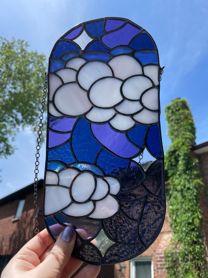 May include: A stained glass window hanging with a chain. The design features white flowers with purple and blue accents.