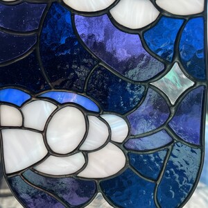 May include: A stained glass window panel with a blue, white, and purple design. The panel is made up of many small pieces of glass that are joined together with lead.