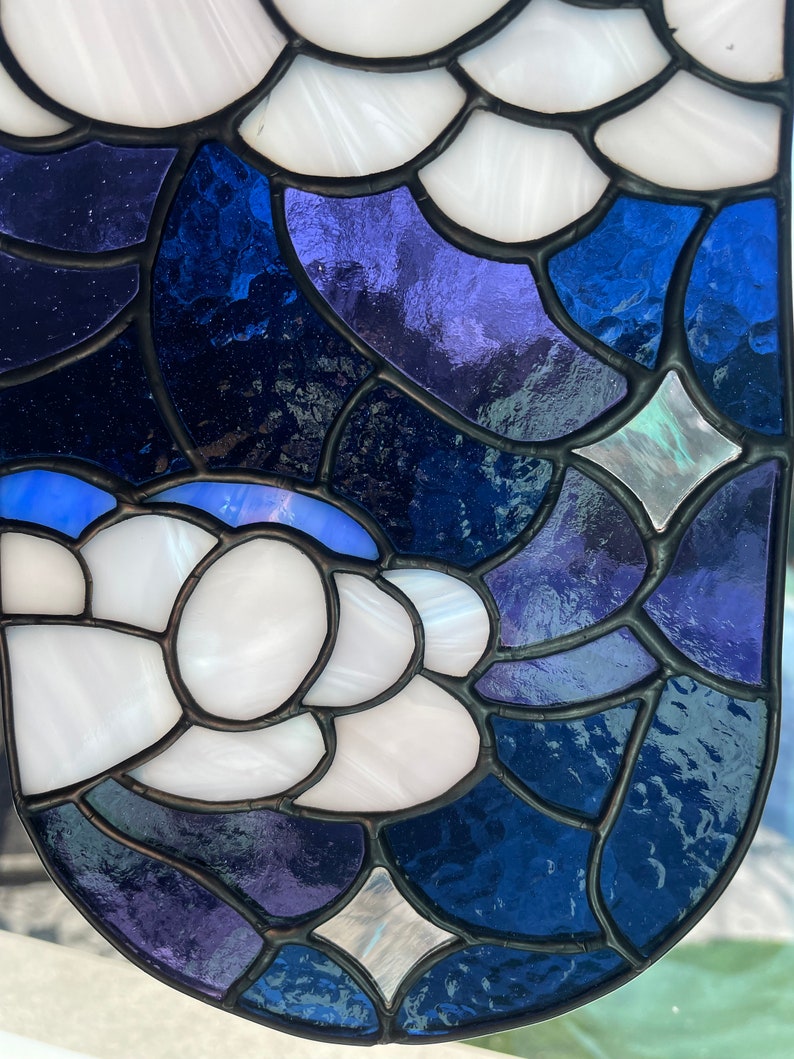 May include: A stained glass window panel with a blue, white, and purple design. The panel is made up of many small pieces of glass that are joined together with lead.
