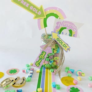 Könnte beinhalten: Ein Glas gefüllt mit bunten Marshmallow-Müsli, verziert mit einem Regenbogen, einem grünen Kleeblatt und Schildern mit der Aufschrift "Free Gold" und "Magic Inside Gold!"