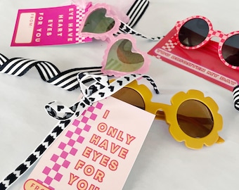 May include: Pink and yellow Valentine's Day gift tags with the text "I only have eyes for you" and "You brighten my day". The tags are tied with black and white ribbon to pink and yellow sunglasses.