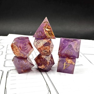 May include: A set of seven resin dice in shades of purple and gold. The dice are in various geometric shapes, including a pyramid, a cube, and a d20. The numbers are in gold. The dice are arranged on a white surface.