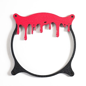 May include: A decorative, black, cauldron-shaped frame with a red, dripping blood design at the top. The frame has a textured appearance and is designed to be hung on a wall. The design is a Halloween or horror-themed decoration.